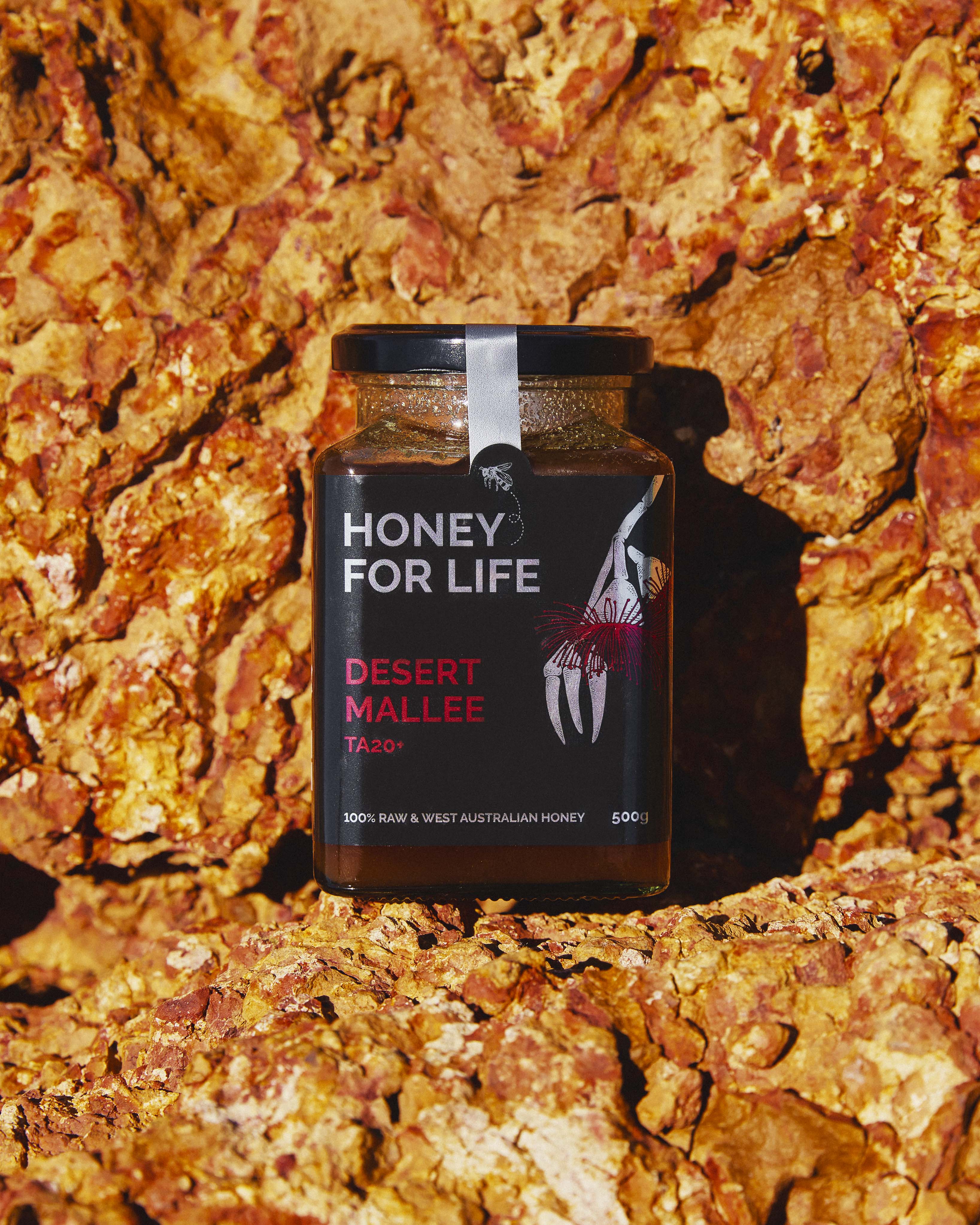 岩の背景に置かれた Honey for Life のデザート・マリー蜂蜜の瓶