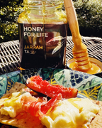 屋外の料理と一緒に皿の上にハニーディッパーを置いた「Honey for Life」とラベルされた蜂蜜の瓶